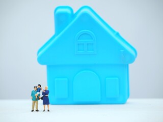 Mini toy of action figure at table with blurred background. Miniature photography concept design. Minifigure of father, mother and children character with house. Happy family concept.