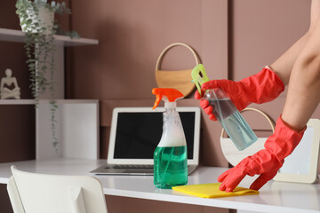 Young woman cleaning desk with rag and detergent at home, closeup
