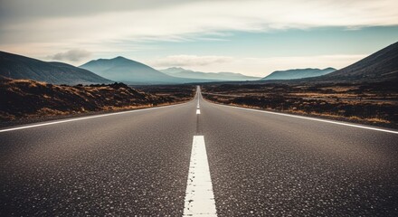 Naklejka premium An endless asphalt road stretches through a vast, arid landscape, leading towards a majestic mountain range on the horizon