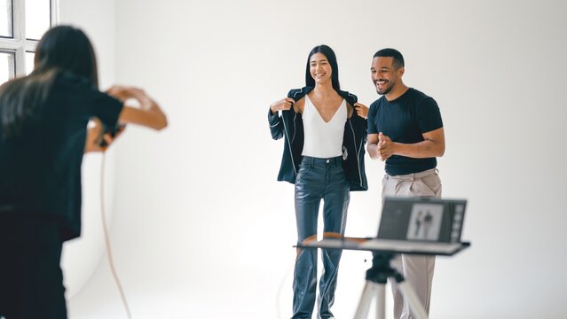 Photographer taking pictures of two fashion models posing in a professional studio, using a digital camera and a tethered setup
