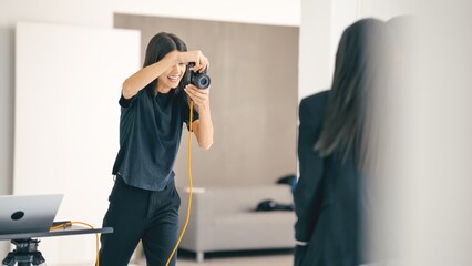 Professional photographer taking pictures of a businesswoman during a photoshoot in a modern studio, using a digital camera and laptop