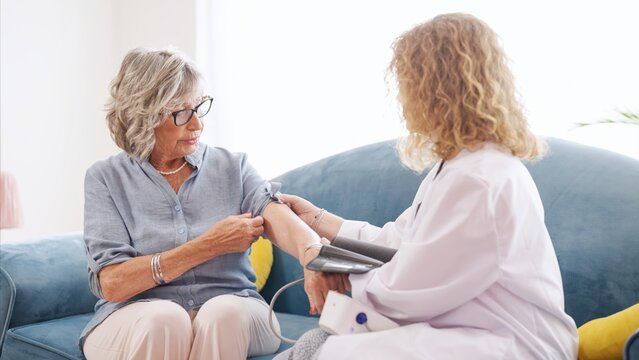 Doctor checking blood pressure of elderly woman using a sphygmomanometer during a home visit, providing essential healthcare support