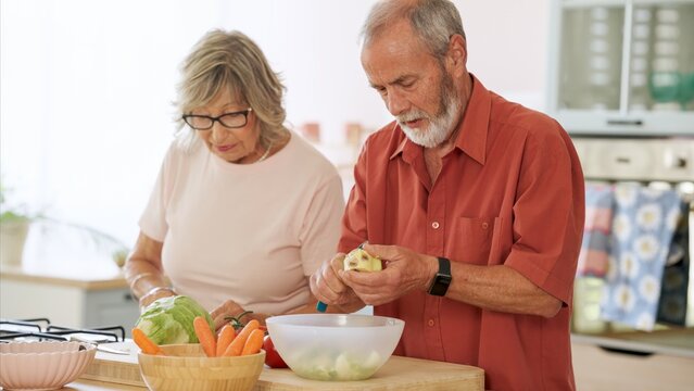 Elderly couple peeling and cutting vegetables, enjoying a healthy lifestyle and preparing a meal together in their kitchen
