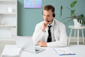 Naklejka premium Young male doctor with laptop giving consultation online in clinic