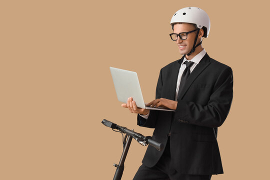 Young businessman with laptop on electric scooter against beige background