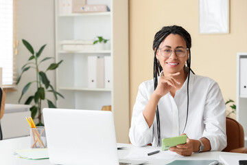 Young African-American woman with calculator and laptop paying taxes online at home