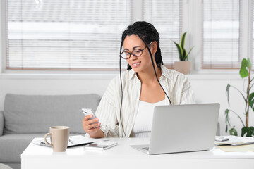 Young African-American woman with mobile phone and laptop paying taxes online at home