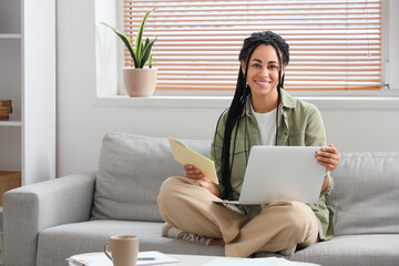 Young African-American woman with tax form and laptop paying taxes online at home