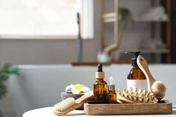 Tray with different massage brushes, sea salt, flower and cosmetic products on table in bathroom