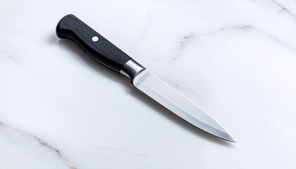 A large black chef's knife is diagonally placed on a white marble surface, highlighted by bright studio lighting.