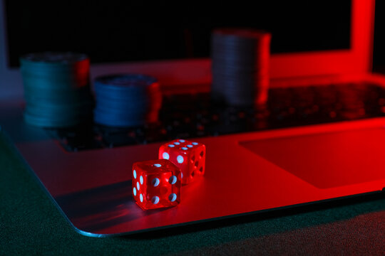 Laptop with poker chips and dices on green table, closeup