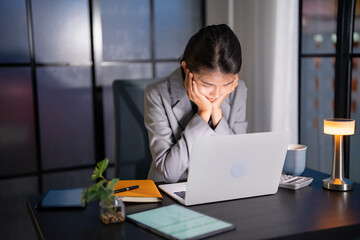 Alone Working Late at Night. Asian business woman at workplace in office late night work at a desk in a dark office working on a laptop late in the evening.