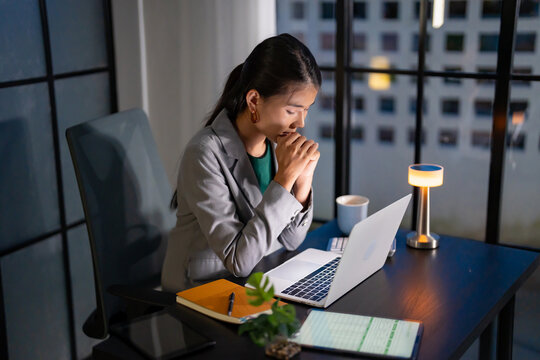 Alone Working Late at Night. Asian&nbsp;business woman at workplace in office late night work at a desk in a dark office working on a laptop late in the evening.