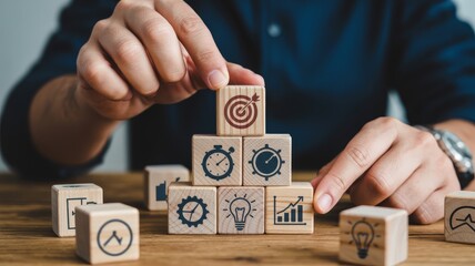 Individual arranges wooden blocks with business icons into a pyramid structure representing achievement