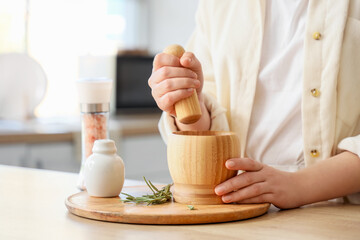 Woman grinding rosemary in mortar at table, closeup
