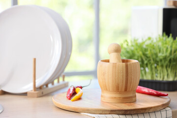Wooden mortar with pestle and hot chili peppers on counter in kitchen, closeup