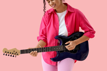 Pretty young African-American woman playing electric guitar on pink background