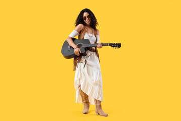Happy young African-American woman with acoustic guitar on yellow background