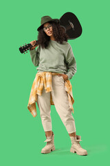 Pretty young African-American woman with acoustic guitar on green background
