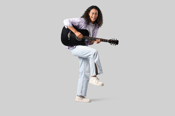 Happy young African-American woman playing acoustic guitar on white background