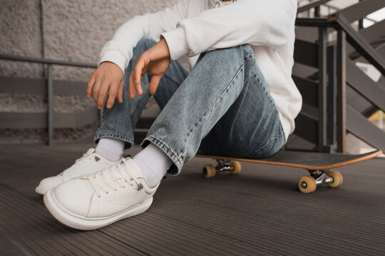 Young man sitting on skateboard outdoors, closeup - Powered by Adobe