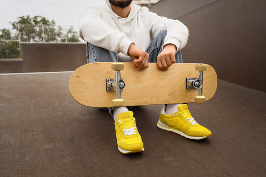 Young man with skateboard sitting at skatepark