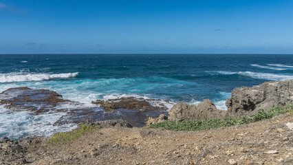 The waves of the blue ocean are raging and crashing against the coastal rocks. White foam on the...