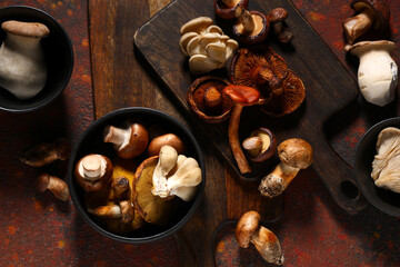 Bowls with different fresh mushrooms on red grunge background