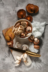 Bowl with different fresh mushrooms and knife on grey grunge background