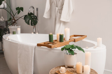 Bathtub with tray and burning candles in bathroom