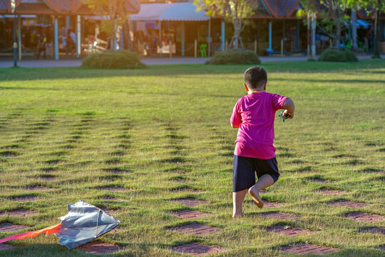 Happy young boy running across grassy field and pulling string of colorful kite. A young child having fun flying kite on windy day in open green space. Joyful moment of childhood play and freedom.