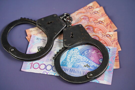 Banknotes of Kazakhstani tenge and handcuffs on a paper background. Fraud, corruption and bribery. Financial fraud.