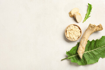 Bowl of horseradish sauce with root, slices and leaf on light background