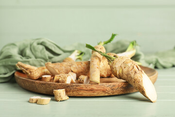 Wooden plate with horseradish roots and slices on green wooden background