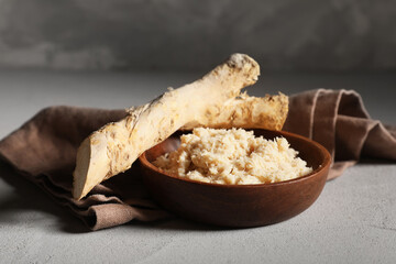 Bowl of horseradish sauce with root on grey grunge background