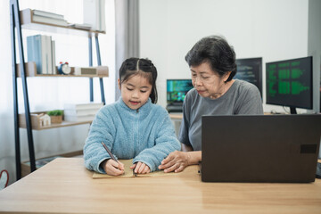 Caring grandmother helping young granddaughter with homework in a cozy home office setting, showcasing intergenerational bonding and learning moments