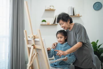 Grandmother and granddaughter enjoying painting together at home, creating memories and fostering creativity in a calm indoor environment
