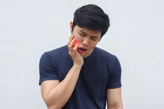 close up young asian man frown and use hand to massage on cheek after feeling pain or hurt from tmj muscle symptom at home for un healthy lifestyle and treatment concept