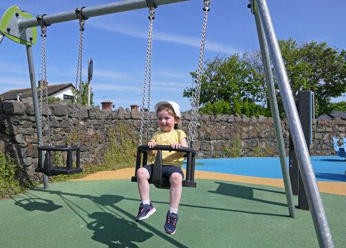 Small girl smiling and having fun on a swing at a playpark on a sunny day in the UK