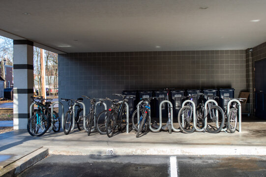 Covered Outdoor Bike Rack with Bicycles Parked Next to a Row of Blue Recycling Bins Under a Shelter.