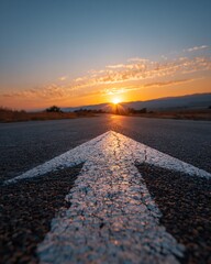 Dramatic Sunset Over Asphalt Road with White Arrow Leading to Horizon in Rural Landscape