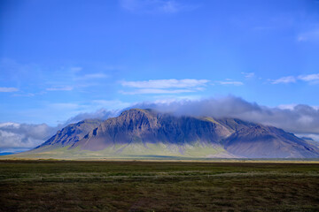 Jagged mountain peaks shrouded in low clouds over dark moorland in Iceland
