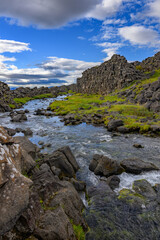 Thingvellir National Park Öxarárfoss waterfall river flowing through the mossy tectonic rift valley under blue sky in Iceland