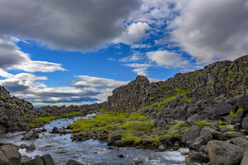 Thingvellir National Park Öxarárfoss waterfall river flowing through the mossy tectonic rift valley under blue sky in Iceland