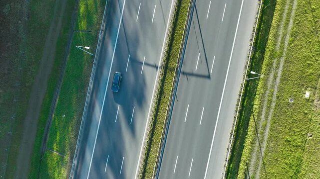 Aerial view of highway with three moving cars casting long shadows across clean asphalt lanes in daylight.