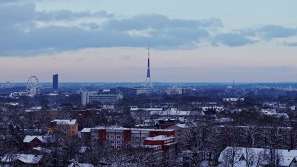 Drone glides forward over snowy Riga rooftops at sunrise with TV tower view - Powered by Adobe