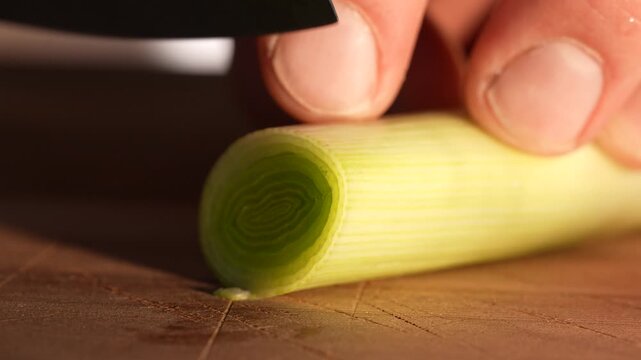 Close-up footage of a fresh leek being sliced on a wooden cutting board. The knife reveals crisp green layers, showing detailed food preparation and clean culinary technique.