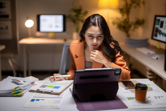 Asian businesswoman working late analyzing data on tablet - Powered by Adobe