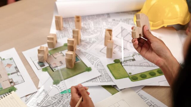Architect and engineer consider or discuss about building construction using blueprint on table with architectural document, measurement tool and wooden block scatter around at office. Delineation.