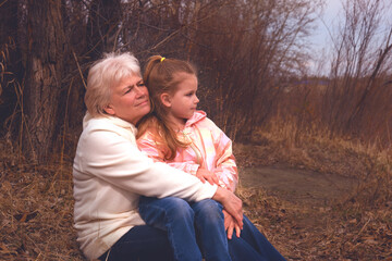 Fototapeta premium Grandmother walking with her granddaughter. Happy family. Having good times with grandparent outdoors. Golden hour, sunset. Love, connection, bonding. Photo exudes warmth and connection